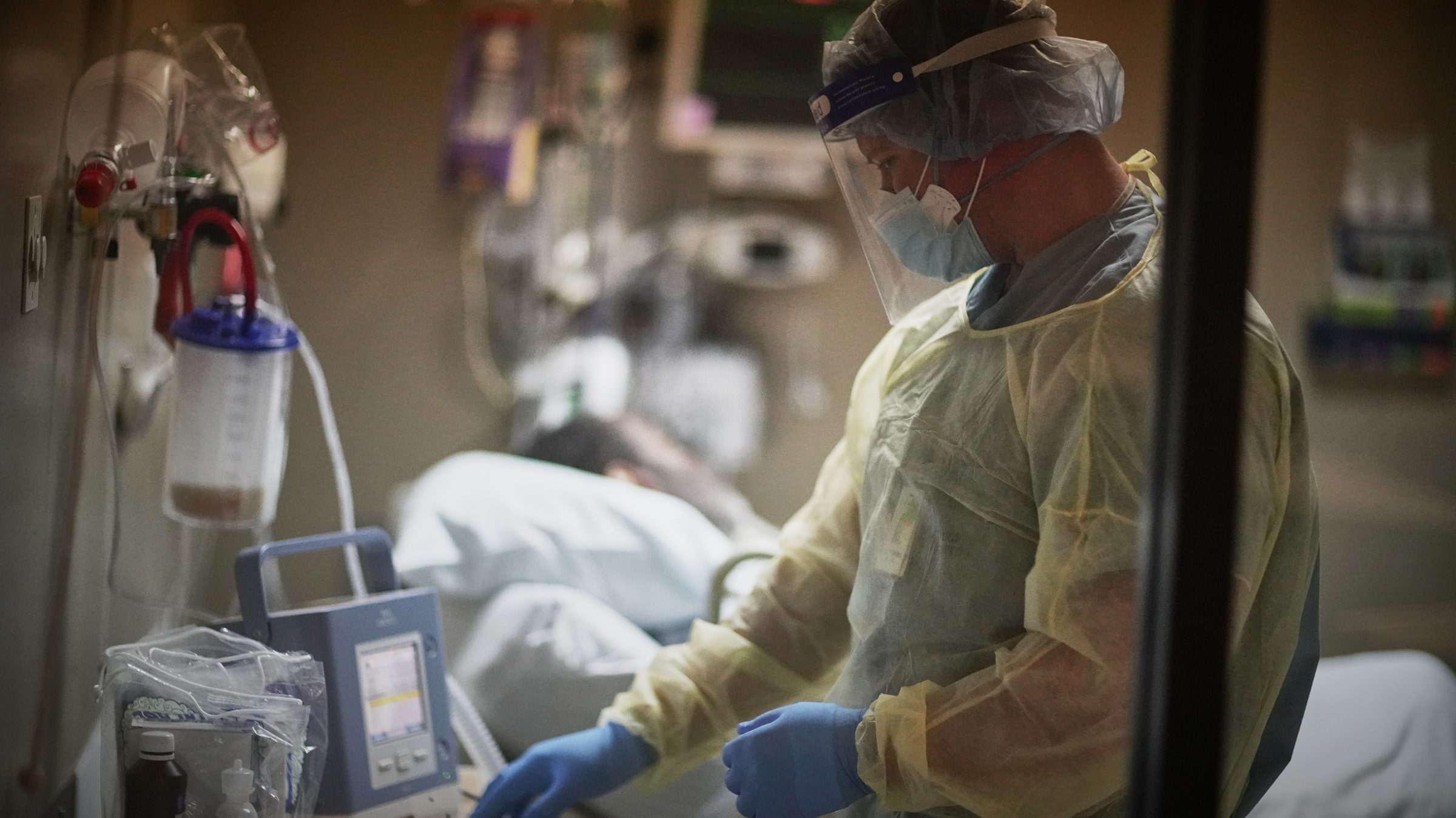 A hospital ICU clinician in full PPE checking a ventilated patient — the endpoint of the nitrile glove supply chain