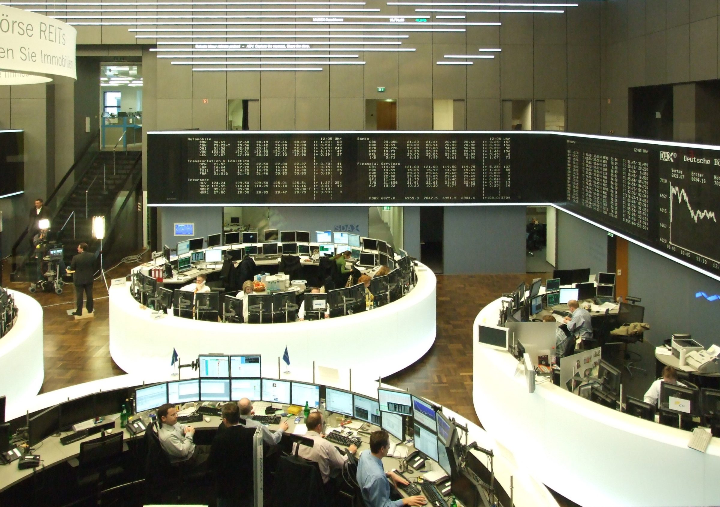 Frankfurt Stock Exchange dealing floor — circular trading desks with traders at multiple-monitor workstations beneath a live ticker wall
